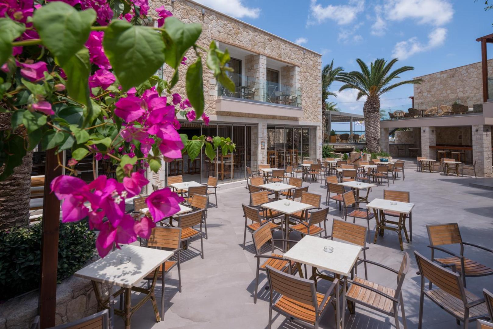 Viesnīcas āra terase ar galdiņiem, krēsliem un ziedošiem bugenvillejas ziediem.