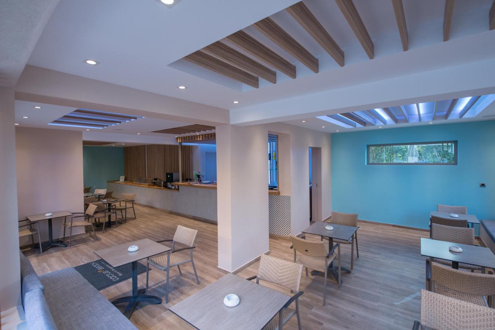 Mūsdienīga atpūtas telpa ar galdiņiem, pītiem krēsliem un gaiši zilu sienu.