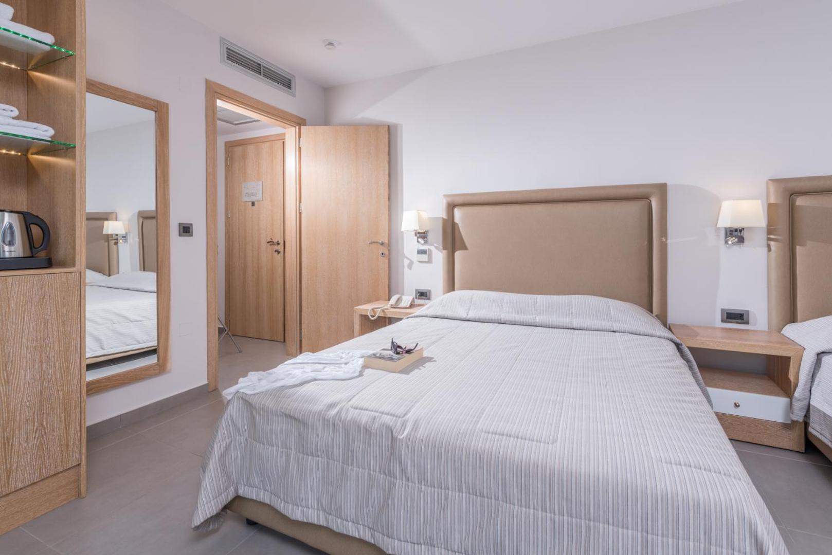 Viesnīcas numura interjers ar divām gultām, spoguli un koka mēbelēm.