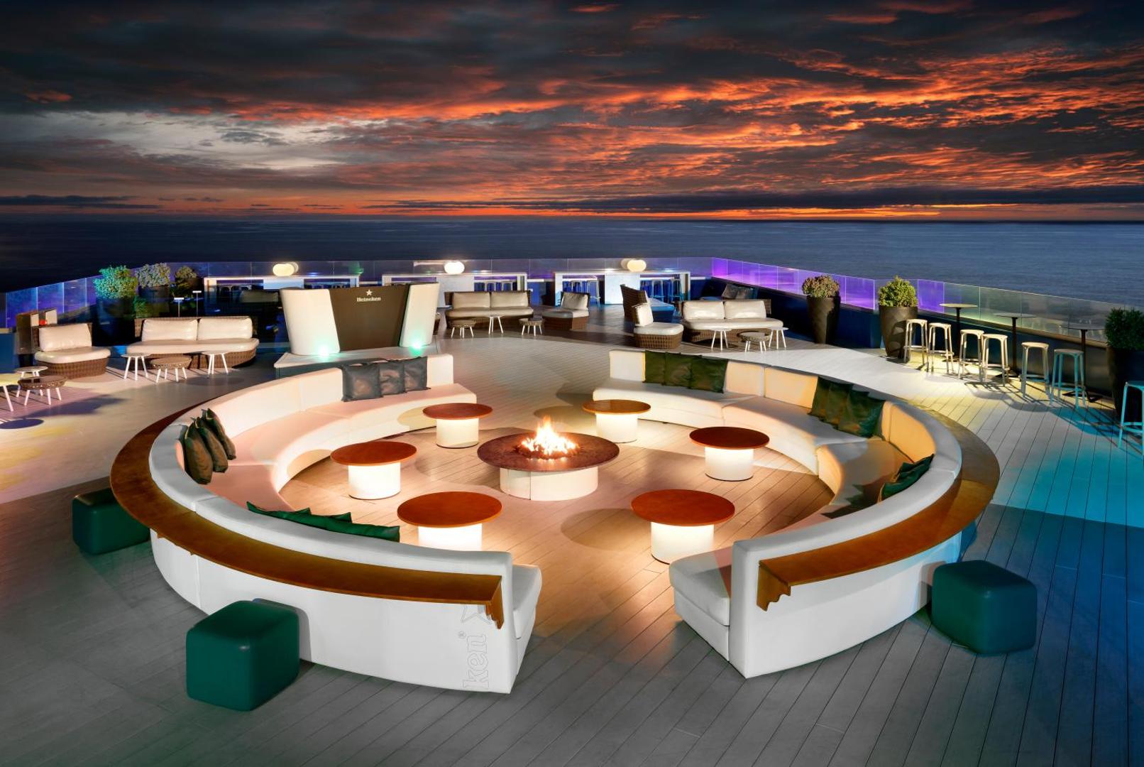 Hard Rock Hotel Tenerife jumta terases bārs saulrieta laikā ar skatu uz okeānu, modernām mēbelēm un ugunskura vietu centrā.