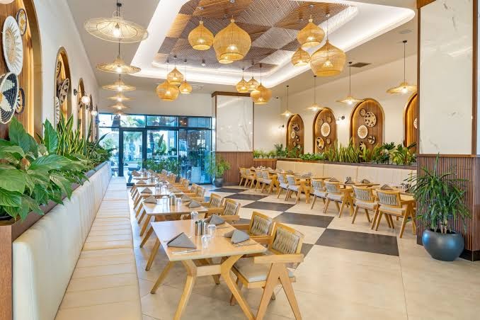 Jacaranda Luxury Resort restorāna iekštelpas ar gaišām koka mēbelēm, dekoratīviem augiem un oriģināliem griestu dekoriem