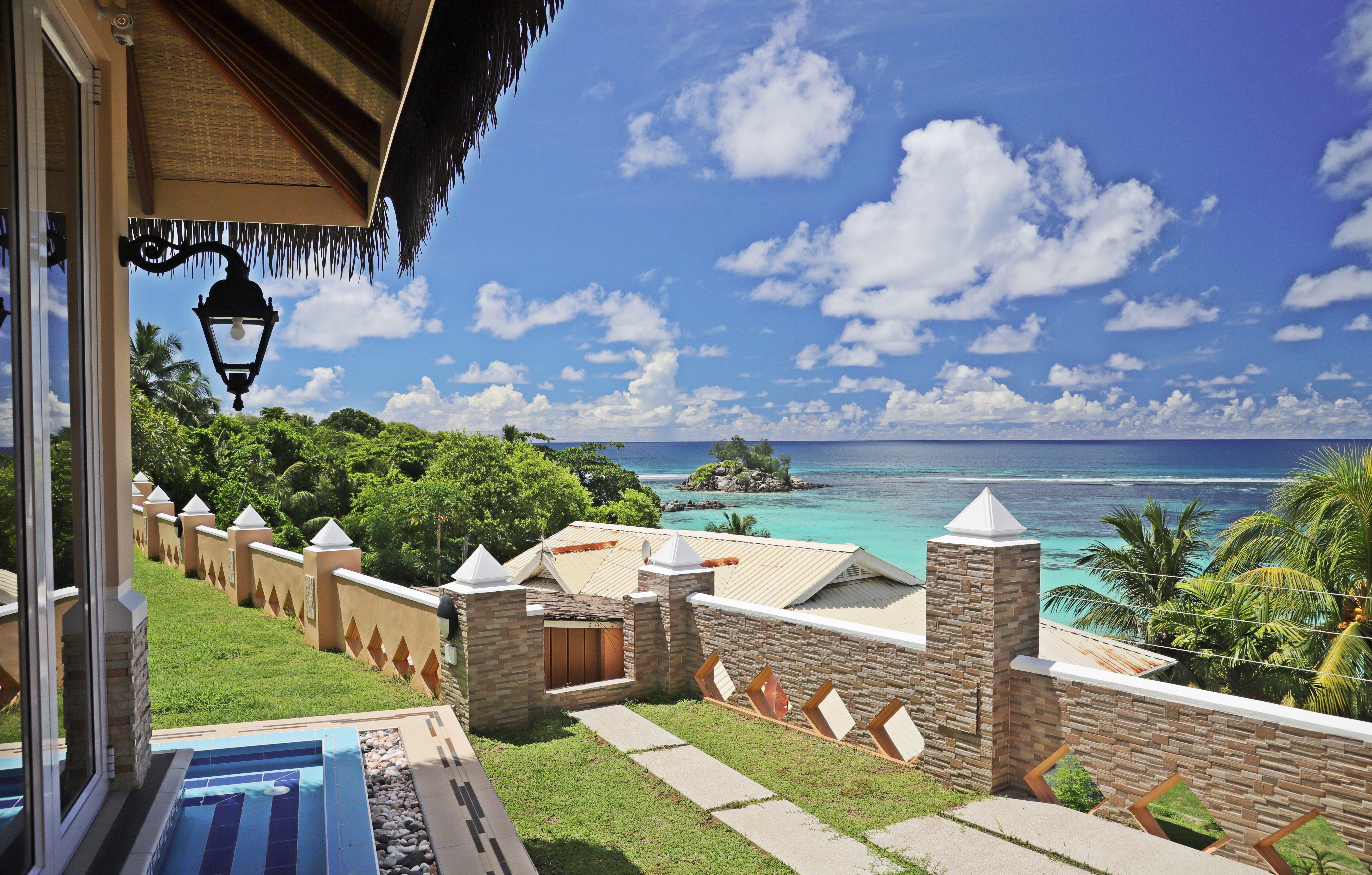 Skats uz tropisko pludmali ar zilu jūru un baltām mākoņu debesīm, redzamas zaļās palmas un ainaviskas villas. Ideāla atpūtas vieta. panoramic view with beach and pools