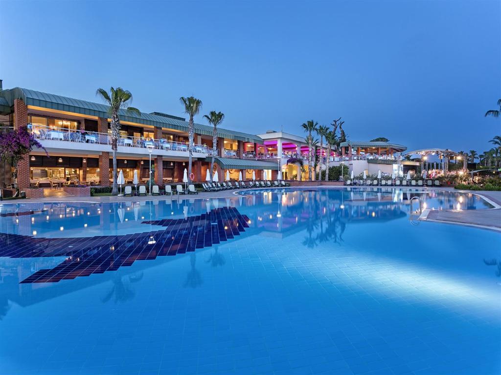 Pine Beach Belek baseins ar viesnīcas ēku piekrastē, vakarā