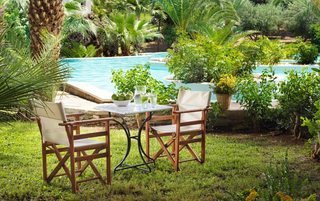 Divi krēsli pie dārza galda ar skatu uz baseinu un zaļumiem.