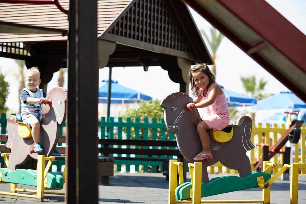 Bērni spēlējas Lindos Princess Beach Hotel rotaļu laukumā uz koka zirgiem.