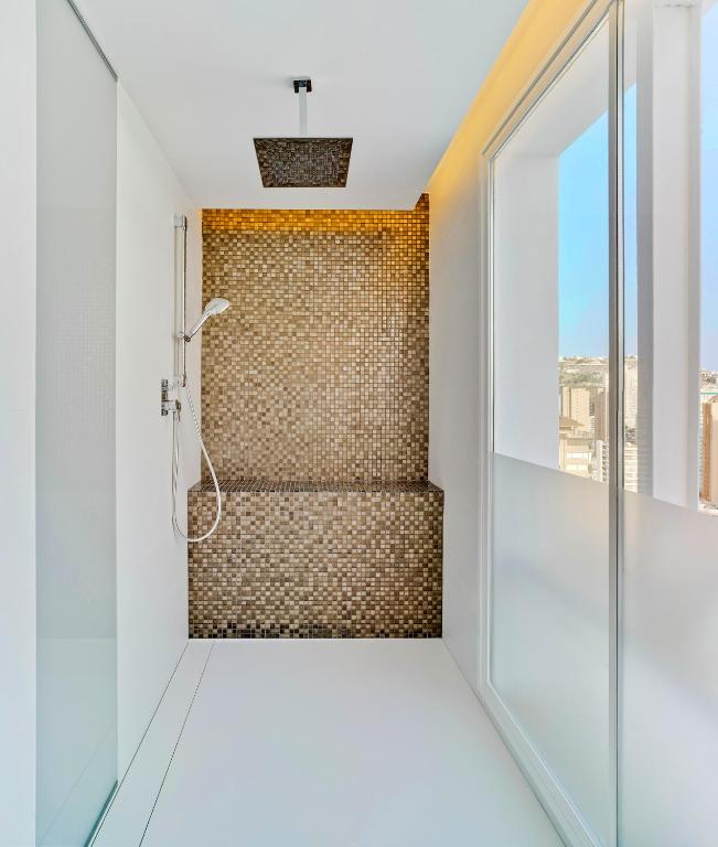 Mūsdienīgs dušas stūrītis ar mozaīkas sienu un lielu griestu dušas galvu, kas piedāvā elegantu un stilīgu izskatu. Gaisma un skats no loga padara to par pievilcīgu vietu relaksācijai.