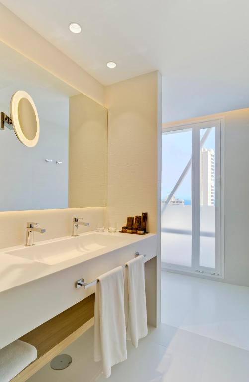 Moderns vannas istabas interjers ar divām izlietnēm, spoguli un skatu uz pilsētu. Gaismas elementi un minimālistisks dizains rada elegantu atmosfēru.