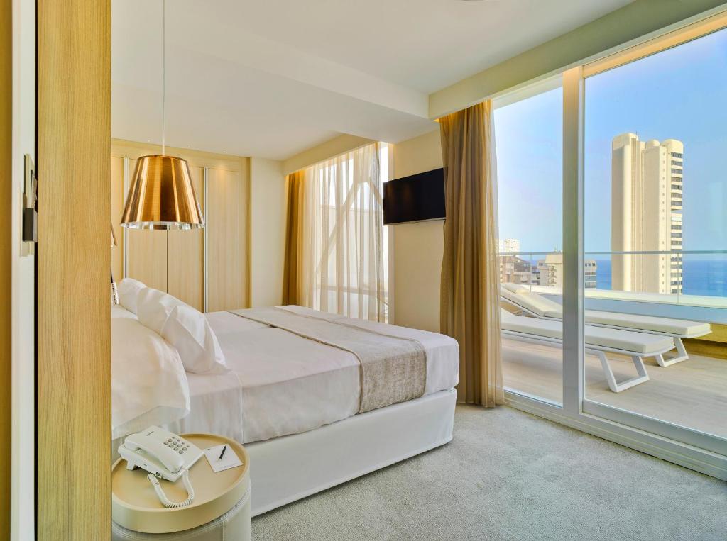 Mūsdienīgs viesnīcas numurs ar plašām logiem un skatu uz jūru, iekārtots ar gultu, televizoru un modernu apgaismojumu. Komfortabla atmosfēra un stilīgs interjers.