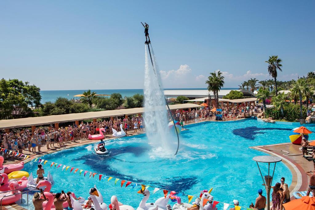 Pine Beach Belek viesnīcas baseins ar ūdens sporta izrādi un viesiem piekrastē.