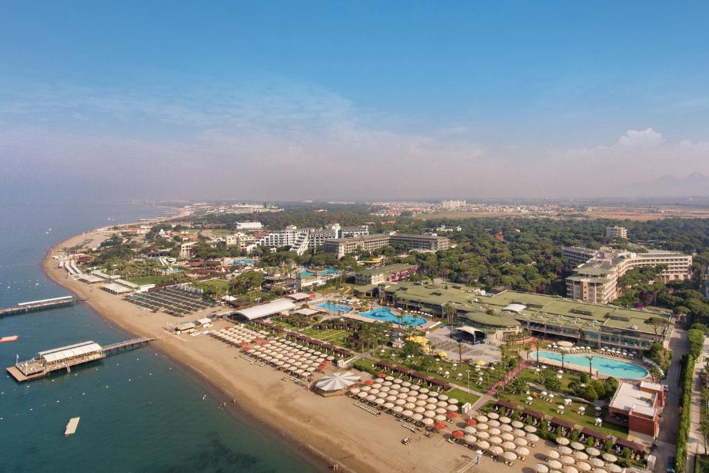 Gaisa skats uz Pine Beach Belek viesnīcu piekrastē ar peldbaseiniem un pludmali.