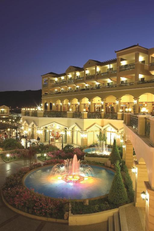 Lindos Princess Beach Hotel piekrastes ainava ar strūklaku un apgaismojumu.