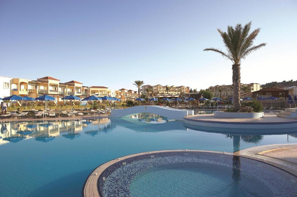 Viesnīcas Lindos Princess Beach Hotel baseins ar palmu un sauļošanās krēsliem piekrastē.
