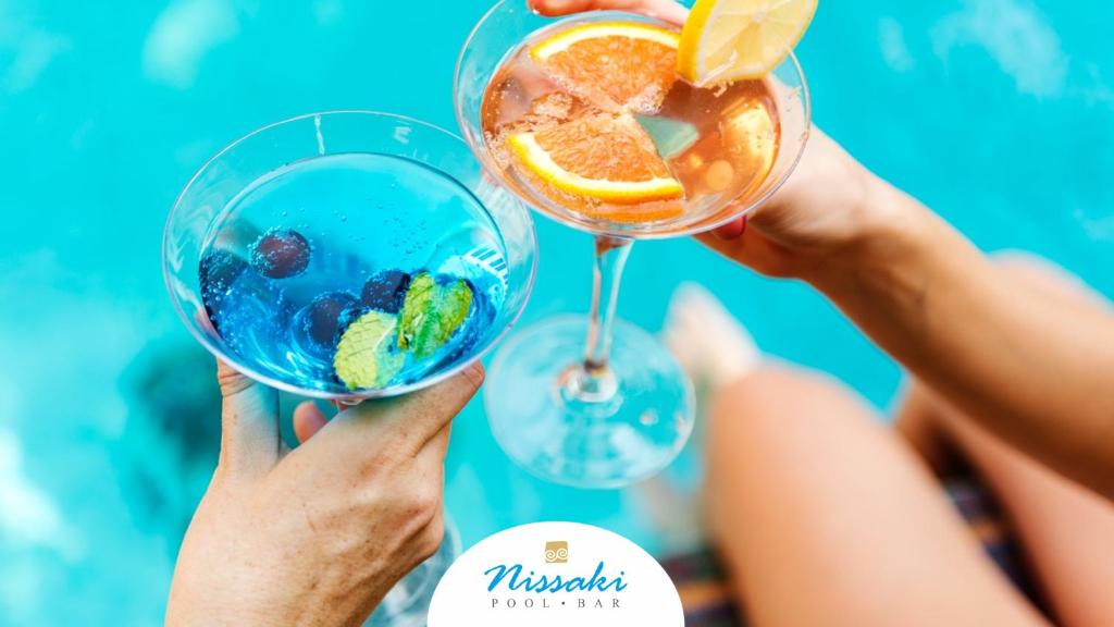 Divi kokteiļi Nissaki Pool Bar piekrastē, vienā roka zils dzēriens, otrā - ar apelsīnu
