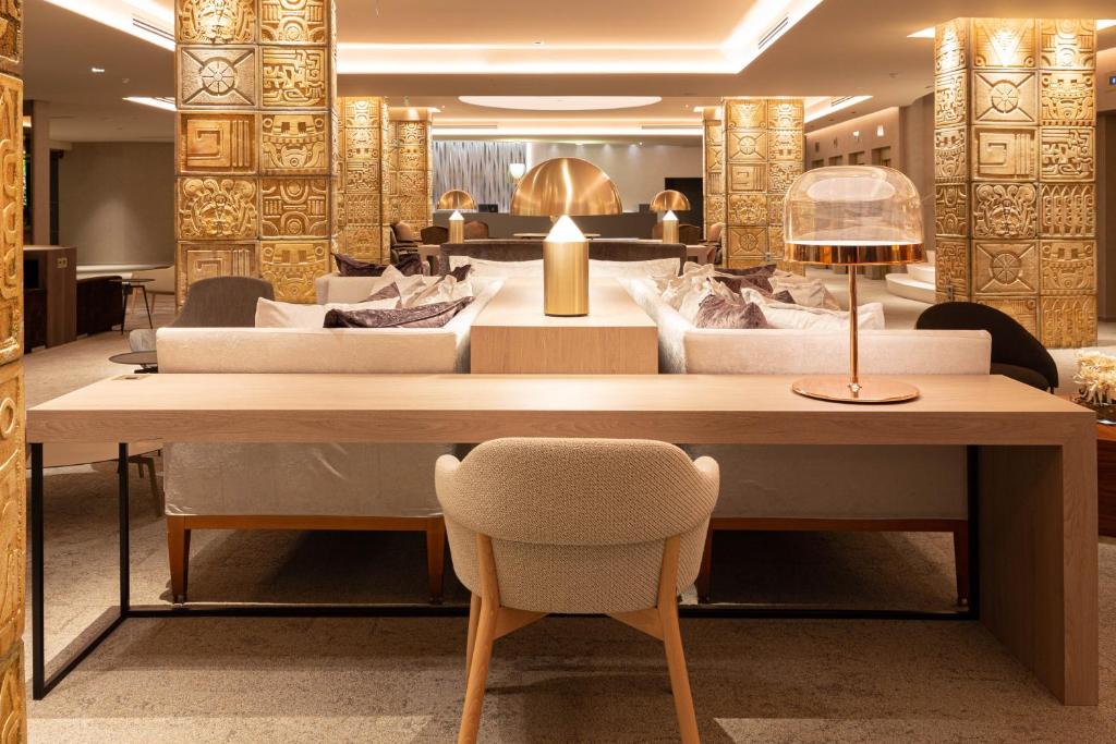 Mūsdienīgs un elegants viesnīcas vestibils ar dekoratīvām zeltītām kolonnām, komfortablām dīvānu zonām un stilīgu galdniecību. Interjers apvieno modernās un tradicionālās dizaina elementi.