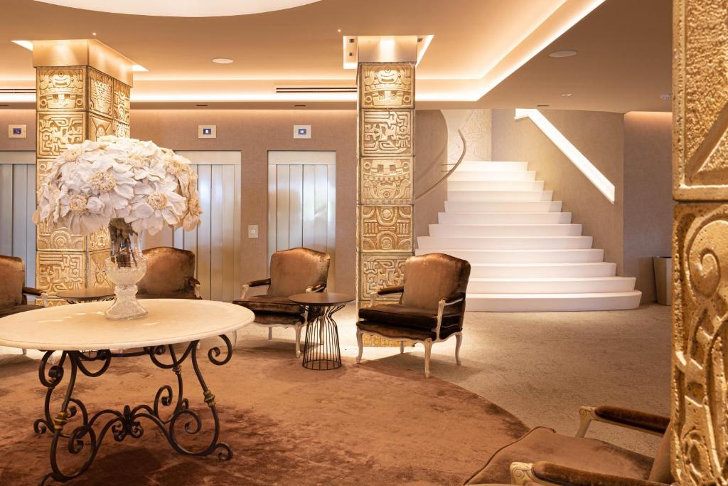 Elegantā viesnīcas halle ar apgaismotām kāpnēm, greznu mēbeļu un dekoratīvu ziedu kompozīciju. Interjers apvieno modernus un klasiskus elementus.