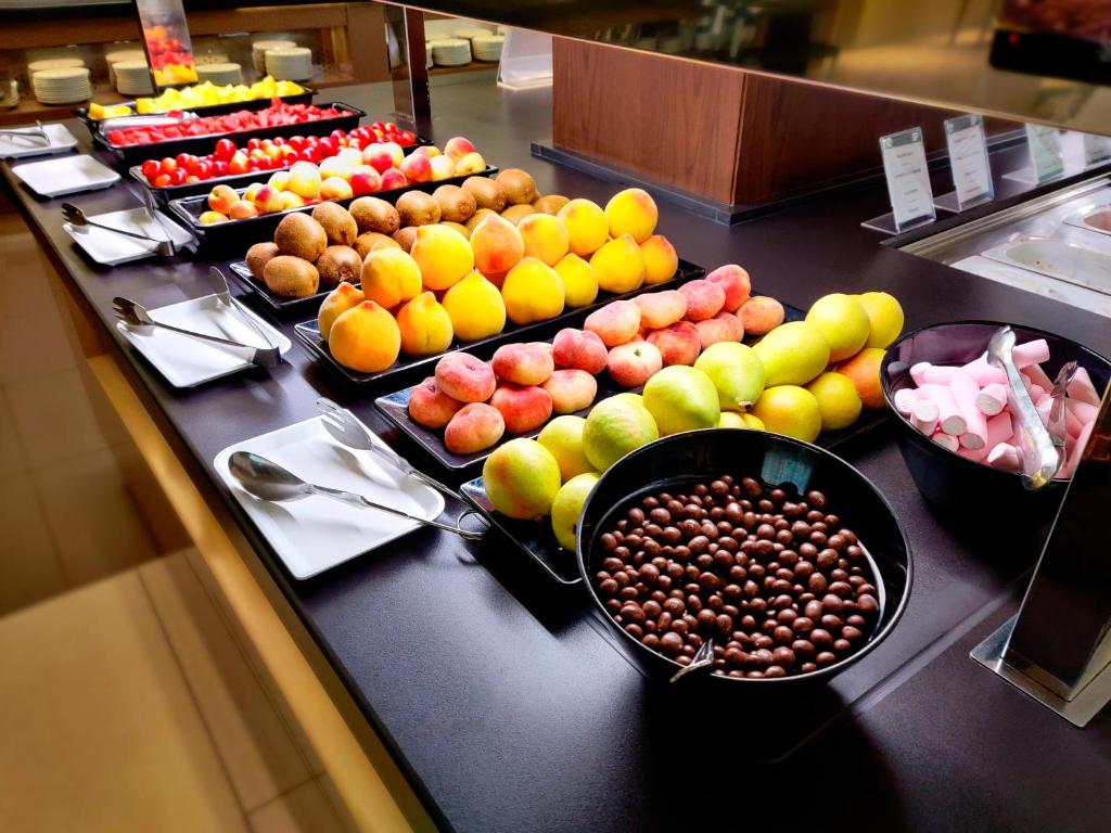 Svaigu augļu un konfekšu bārs ar dažādiem augļiem, tostarp āboliem, bumbieriem un persikiem, kā arī šokolādes un saldumu traukiem. Ideāls izvēles variants veselīgam brokastu vai uzkodu brīdim.