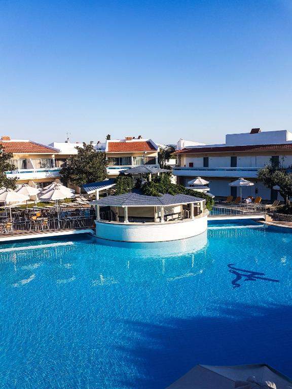 Lydia Maris Resort & Spa baseins ar bāru un viesnīcas ēkām piekrastē.