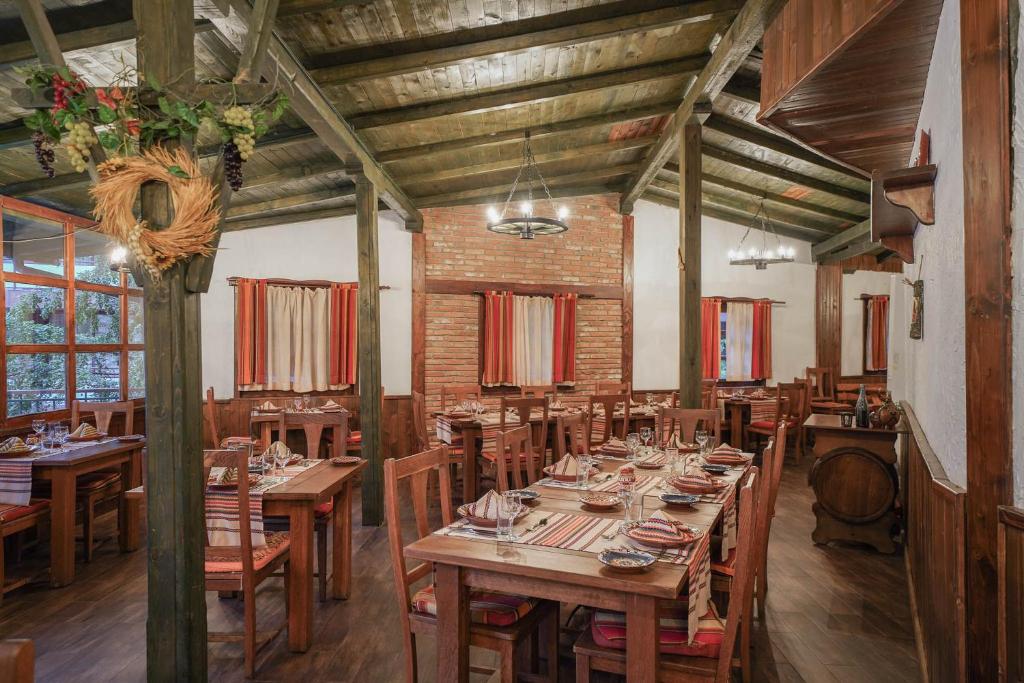 Klasisks restorāns ar koka interjeru un siltu apgaismojumu, kurā redzami galdi ar galda piederumiem un dekoratīvām detaļām. Atmosfēra ir mājīga un aicinoša, ideāli piemērota maltīšu baudīšanai.