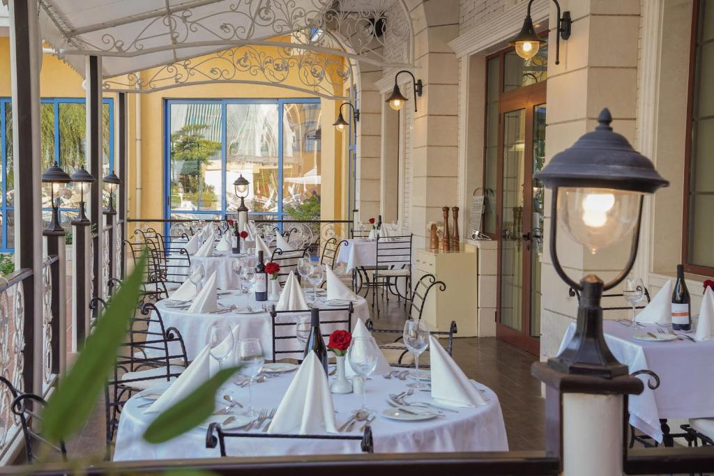 Elegantā restorāna terase ar galdiem, kas klāti ar baltām galdautiem un rotāti ar sarkanām rozēm. Labi apgaismoti apstākļi un viesmīlīga atmosfēra, ideāla romantiskām vakariņām.