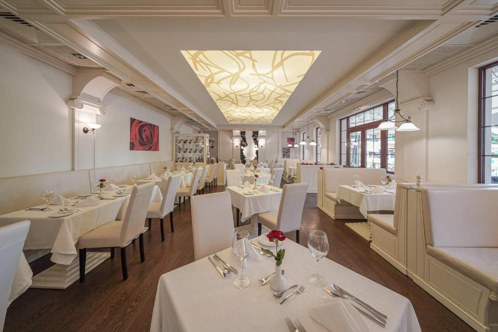 Elegants restorāns ar gaišu interjeru, baltām galdautām un ziedu dekorācijām, kas rada romantisku atmosfēru. Labi izstrādātas detaļas un gaismas elementi piešķir vietai modernu izskatu.