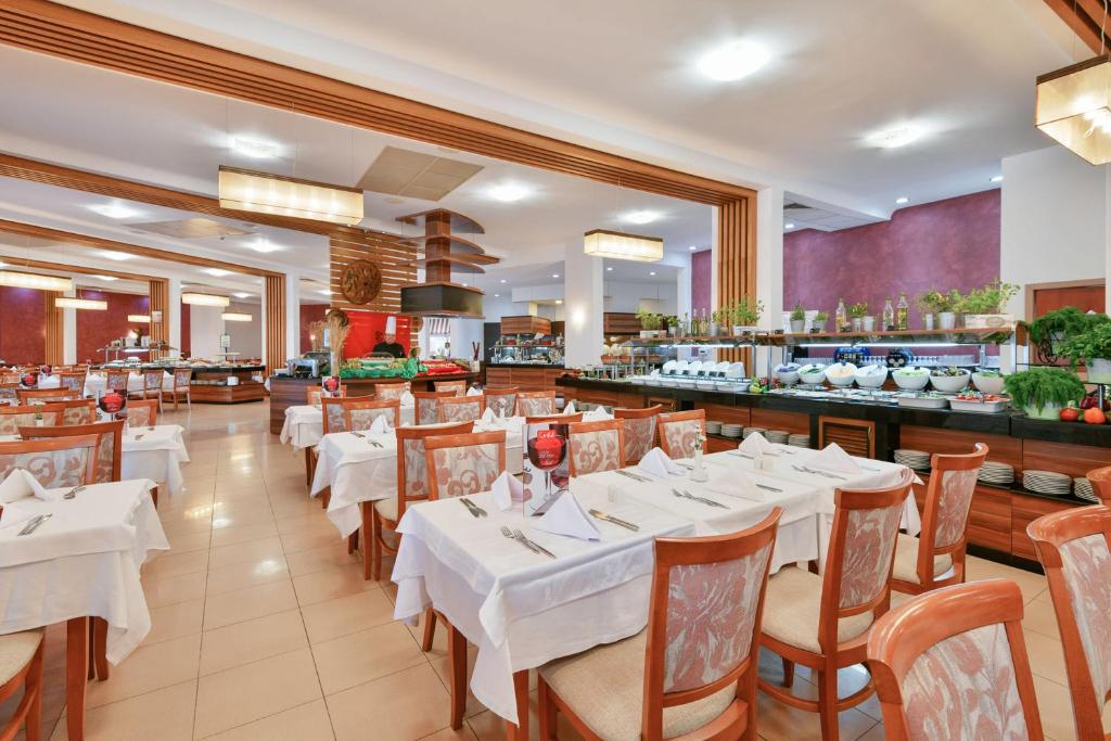 Restorāna interjers ar elegantām galdiem un krēsliem, kas sakārtoti pie bufetes ar dažādiem ēdieniem. Telpa ir gaiša un plaša, radot viesmīlīgu atmosfēru.