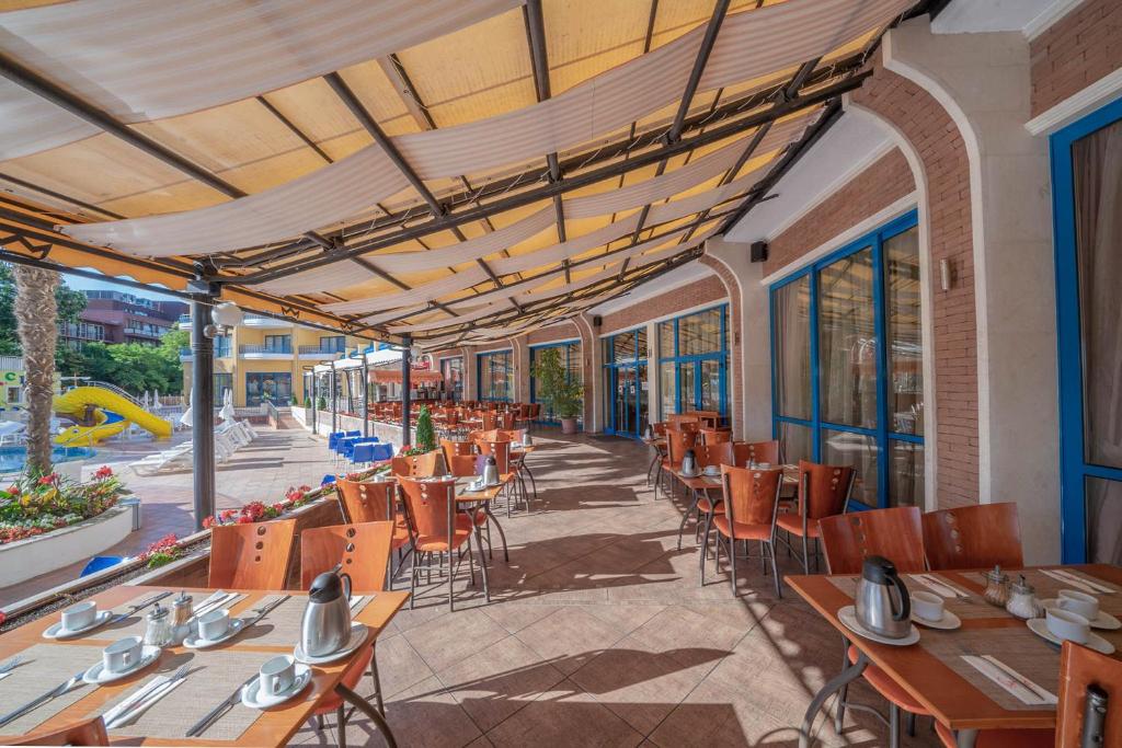 Apsildāmā terase ar galdiem un krēsliem, kas izvietoti blakus baseinam, radot patīkamu atmosfēru ēdienreizei. Gaismas un ēnas spēles piešķir attēlam dzīvīgumu.