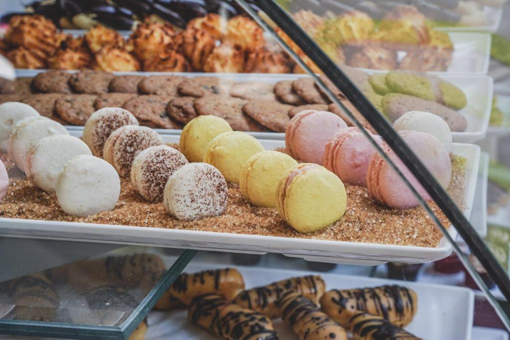 Saldumu vitrīna ar dažādām cepumiem un makaronu šķirnēm, tostarp krāsainiem makaronu izstrādājumiem, kas novietoti uz smilšu kārtas.