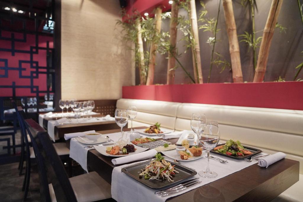 Moderns restorāns ar elegantiem galdiem, kas klāti ar baltām galdautām un šarmantiem traukiem, piedāvā dažādus ēdienus. Interjerā redzami bambusa augi un siltā krāsu palete, radot patīkamu atmosfēru.