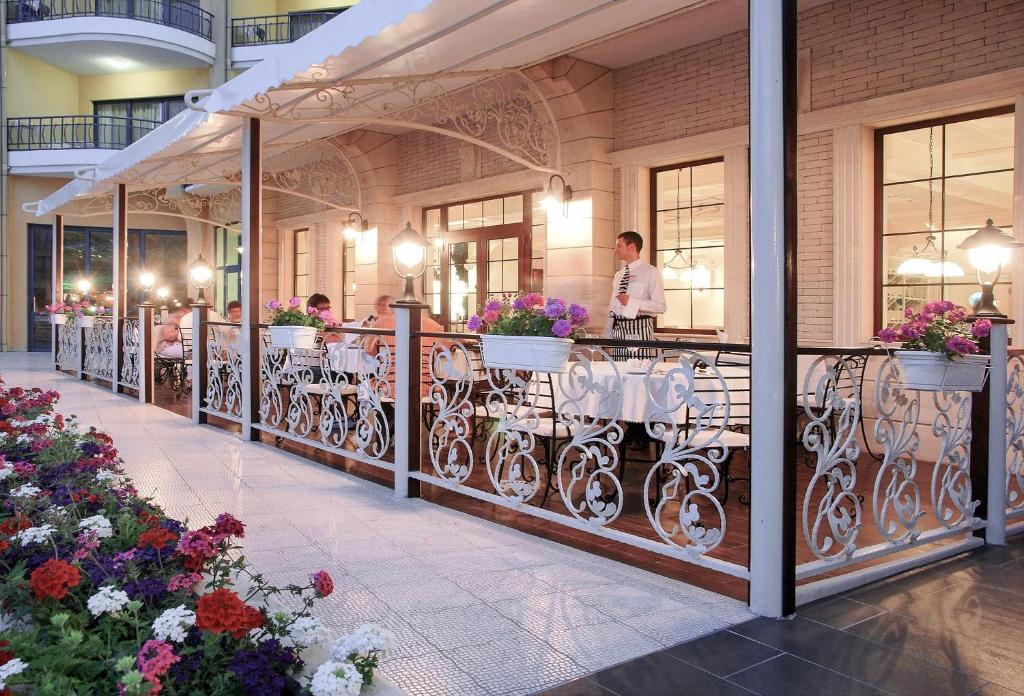 Elegants restorāns ar dekoratīvām margām un ziedu kompozīcijām, kas izveidots ārpus telpām. Apgaismojums rada patīkamu atmosfēru ēdiena baudīšanai.