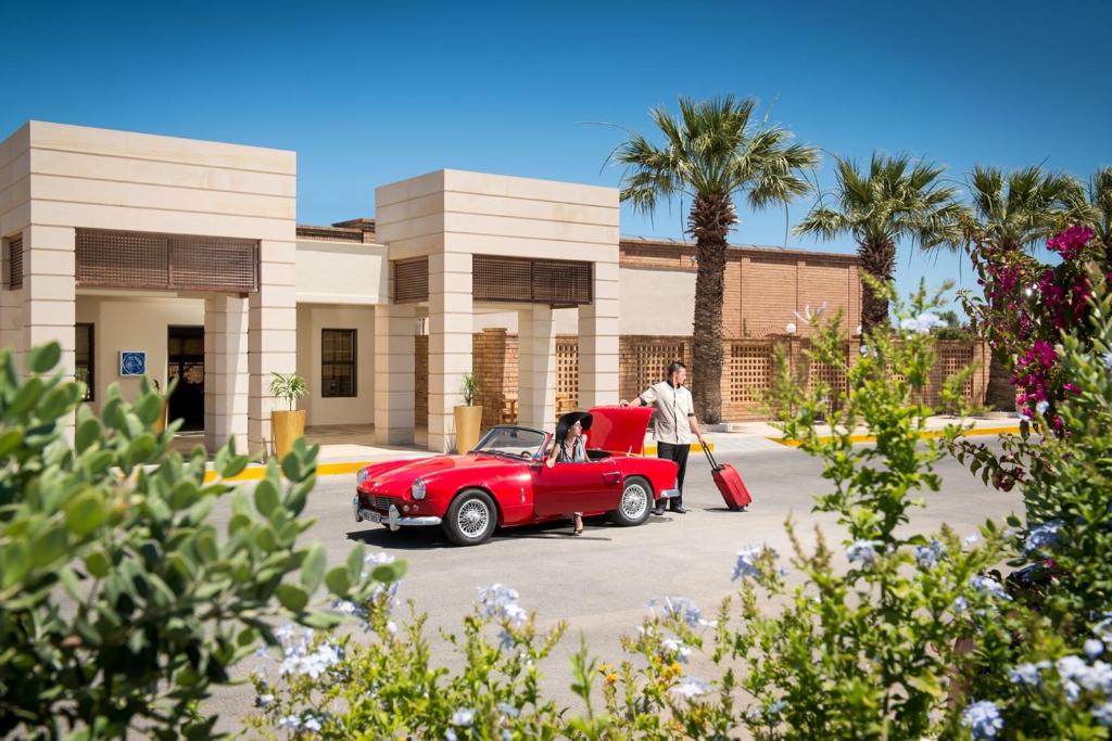 Bella Beach Hotel viesnīca ar elegantām palmām un sarkano auto.