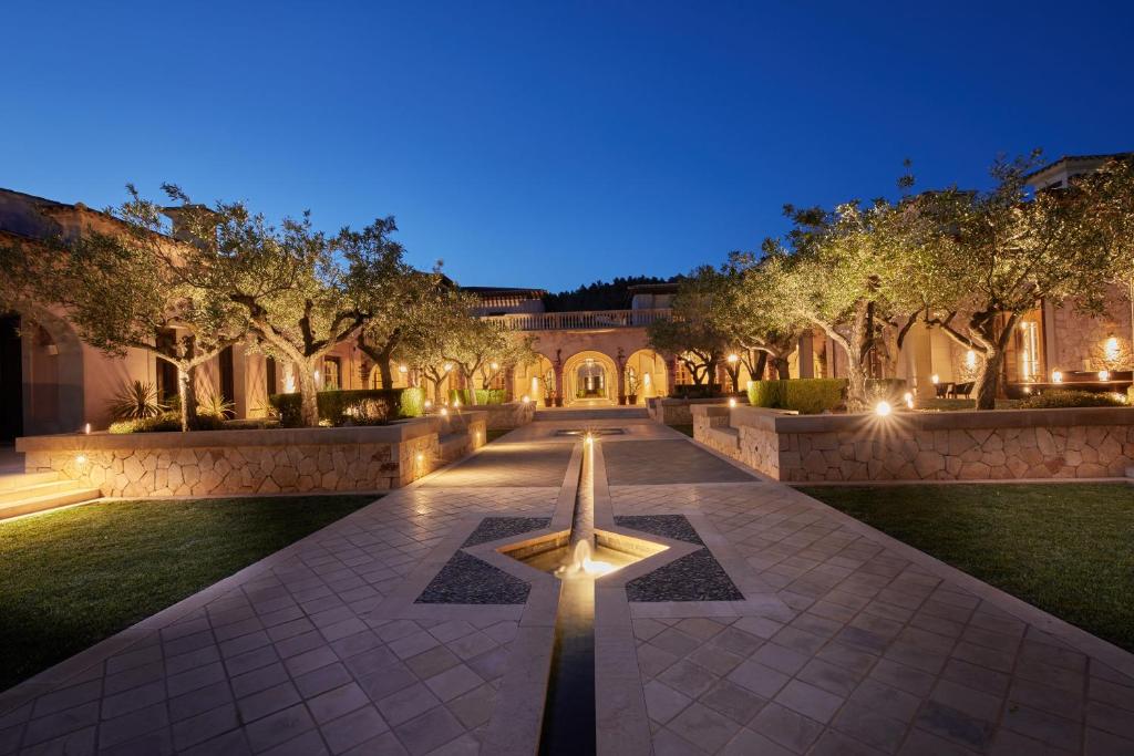 Eleganta viesnīcas iekšpagalms ar apgaismotām olīvkokiem un akmens bruģi, kas radīts mierīgai atmosfērai. Nakts debesīs izceļas mierīgs un grezns vidi.
