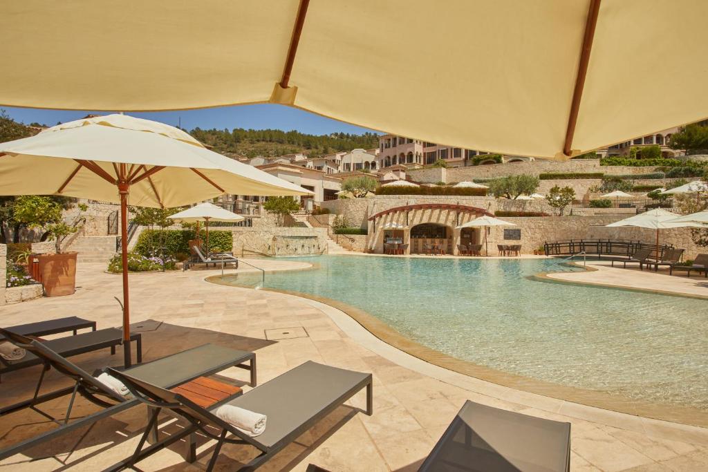 Relaksējošs skats uz baseinu ar sauļošanās krēsliem un saulessargiem, apkārtne izrotāta ar augiem un ainavām. Ideāla vieta atpūtai un relaksācijai.