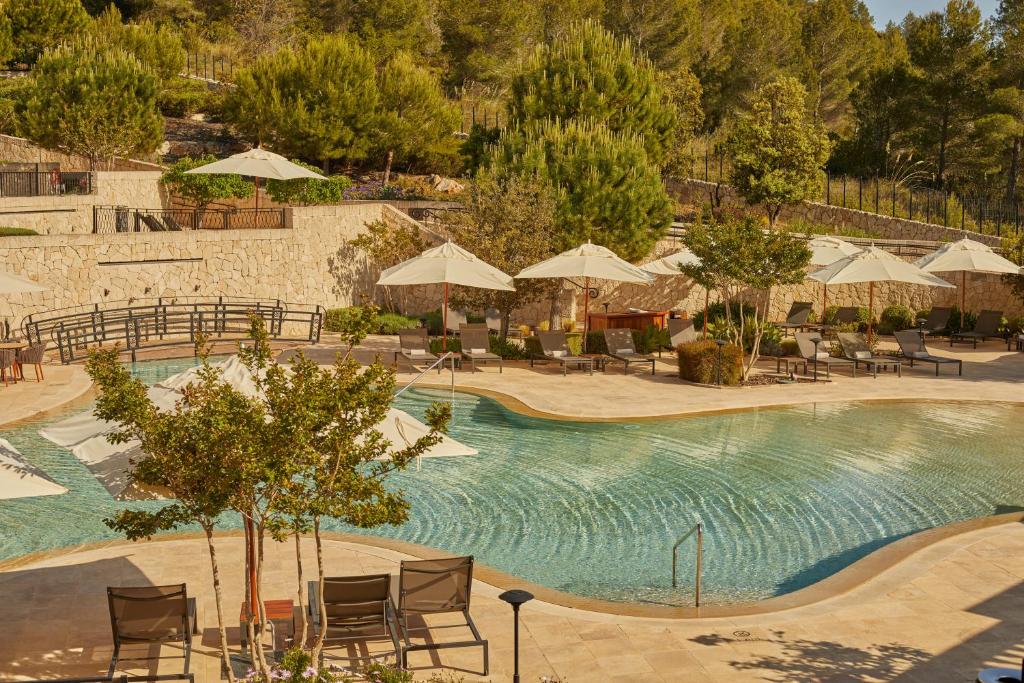 Peldbaseins ar saulessargiem un atpūtas krēsliem, ieskauts zaļajiem kokiem un akmens sienām, radot relaksējošu un mierīgu atmosfēru.