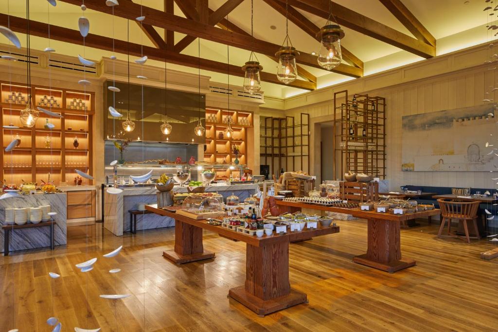 Elegants restorāns ar koka griestiem un gaumīgu iekārtojumu, kurā redzami vairāki galdi ar dažādām ēdienu izvēlēm un smalkiem apgaismojuma elementiem.