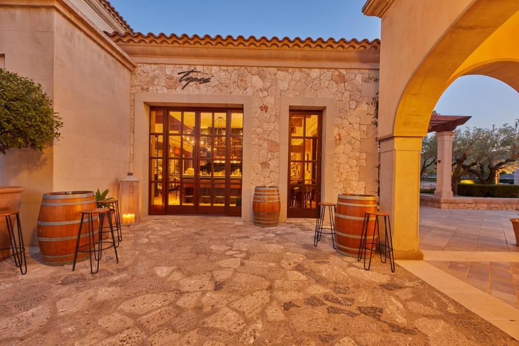 Elegants restorāna ieeja ar akmens sienām un koka durvīm, kur redzami vīna mucas un sveces. Apkārtne ir mierīga un viesmīlīga, radot patīkamu atmosfēru.