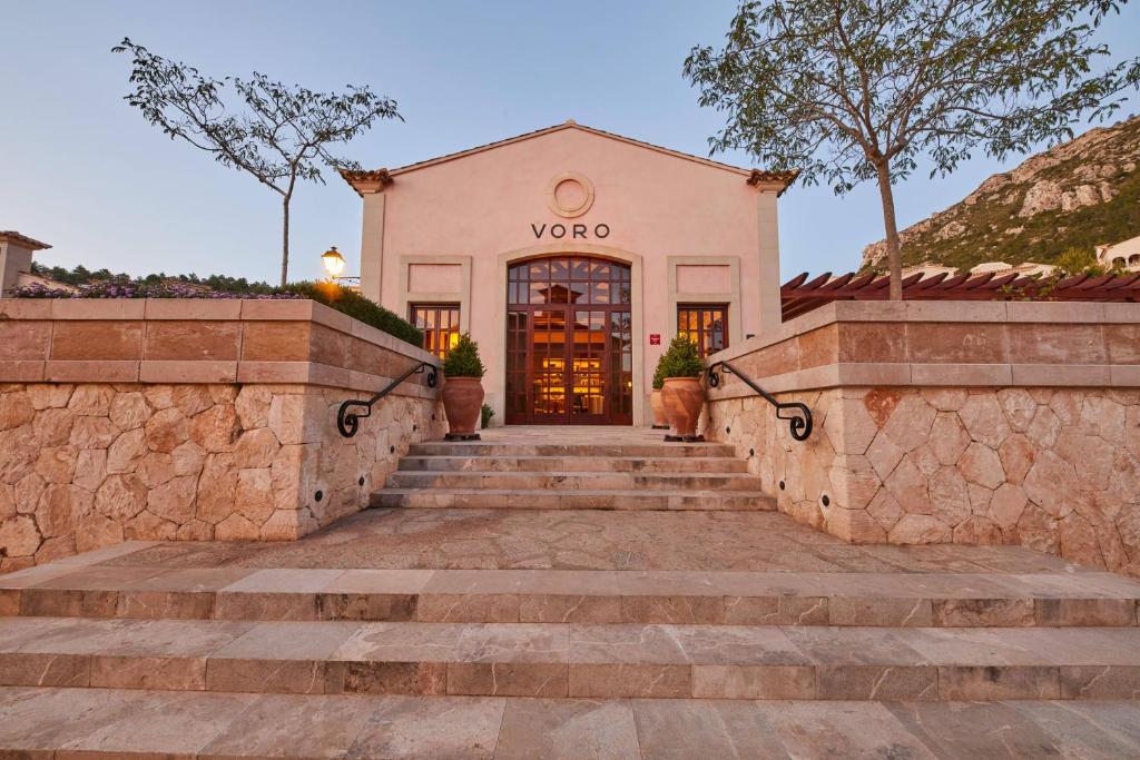 Restorāna Voro ieeja ar akmens pakāpieniem un elegantu fasādi, apzaļumotu teritoriju un kalnu fona.