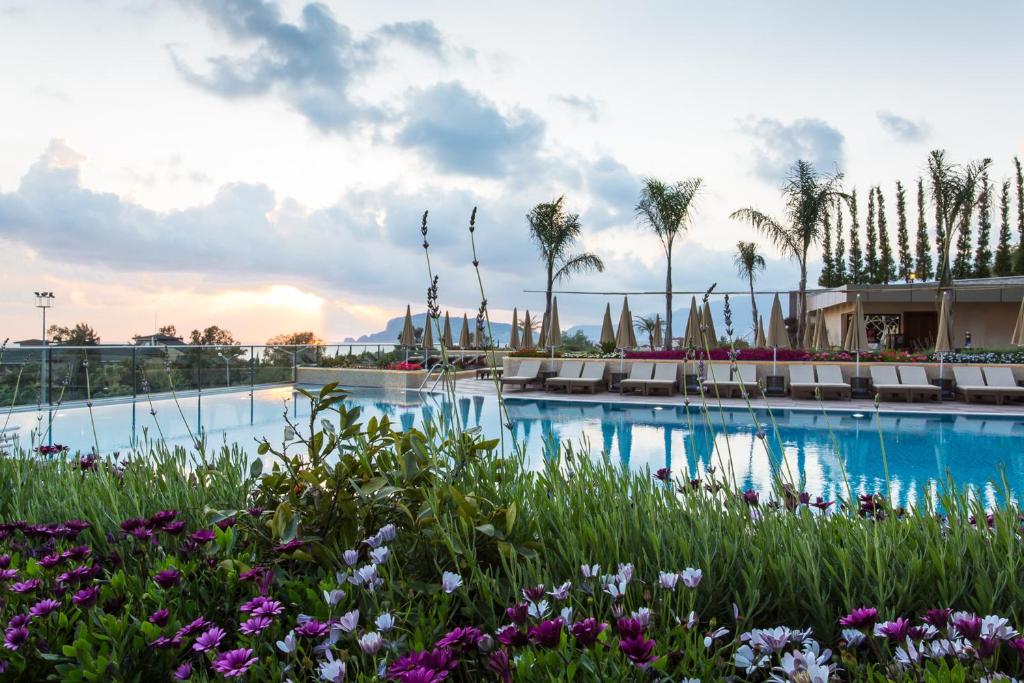 Michell Hotel & Spa baseins ar ziediem un palmām, saulriets piekrastē.