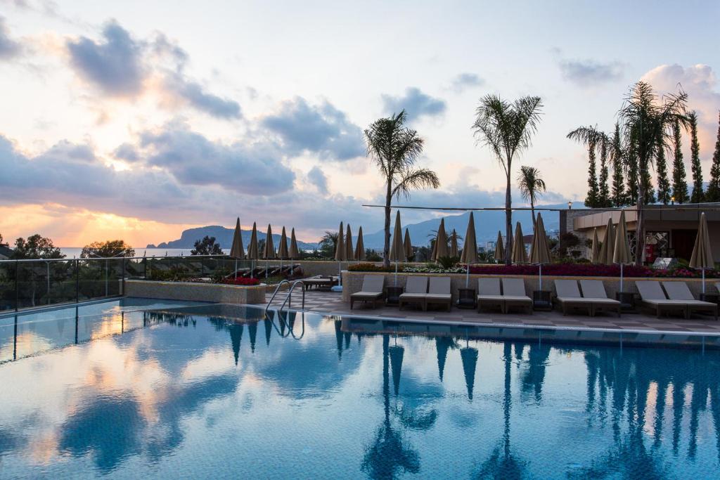 Michell Hotel & Spa baseins ar palmām un saulrietu fonā