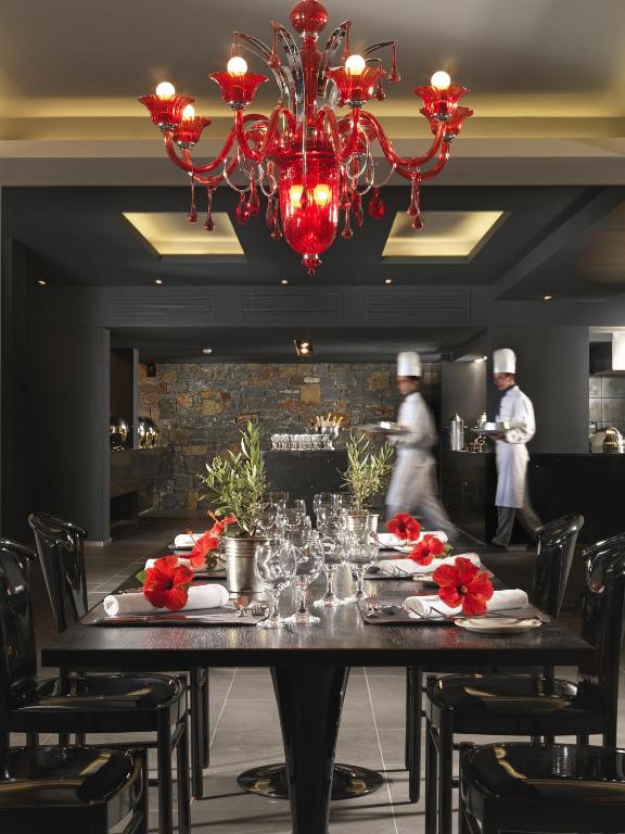 Eleganta restorāna interjers ar sarkanu lustru un ziediem uz galda.