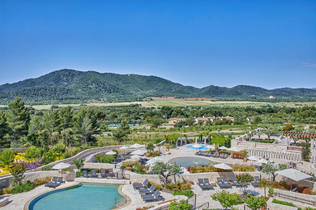 Ainava ar peldbaseinu un kalniem fona, kas sniedz mierīgu un dabīgu atmosfēru. Viegli saulaini laika apstākļi un apzaļumoti dārzi veido relaksējošu vidi.