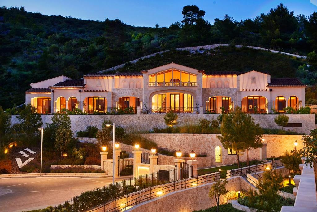 Luksusīga māja ar modernu arhitektūru, apgaismota vakara stundās, ieskauta zaļām ainavām un ainaviskām kalnu ainavām.