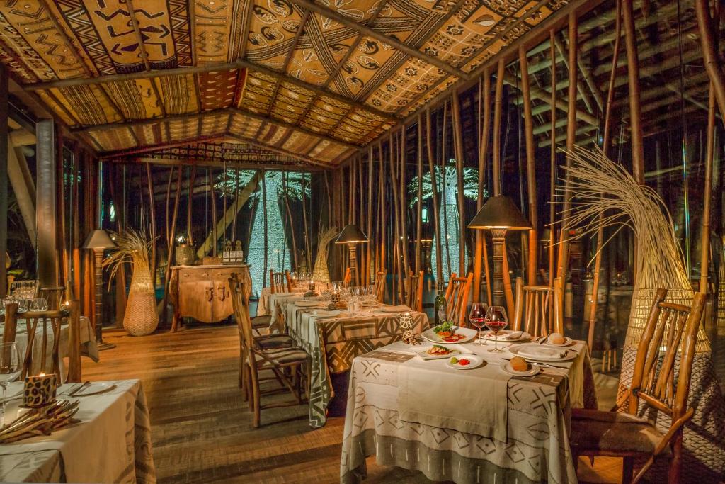 Elegants restorāns ar tradicionālu dekoru, kur galdos ir izsmalcināti ēdieni un vīna glāzes. Interjers apvieno dabu ar māksliniecisku dizainu, radot siltu un viesmīlīgu atmosfēru.
