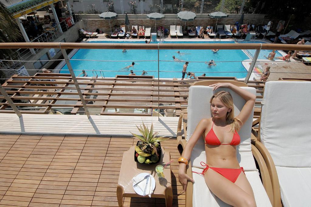 Sieviete sarkanā peldkostīmā atpūšas pie baseina Ambassador Plaza Hotel