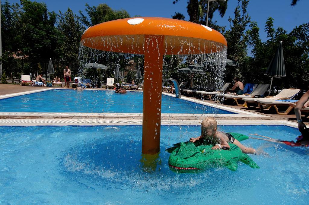 Bērns spēlējas pie baseina Ambassador Plaza Hotel ar zaļo peldriņķi.
