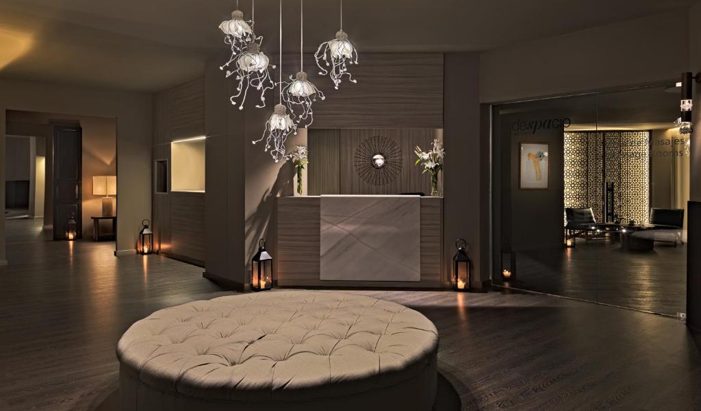Mūsdienīga spa recepcijas zona ar elegantu apgaismojumu un relaksējošu atmosfēru. Interjerā redzama apaļa dīvāna forma un stilīgi gaismas ķermeņi.