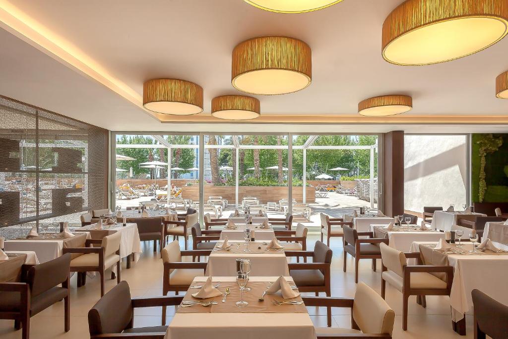 Mūsdienīga restorāna iekārtojums ar elegantiem galdiem un krēslām, kas piedāvā skatu uz āra baseinu un terasi. Apgaismojums rada patīkamu atmosfēru.