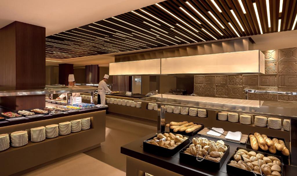 Mūsdienīga restorāna virtuves skats ar plašu bufeti, kurā ir dažādi ēdieni un maizītes. Šefpavārs strādā, sagatavojot ēdienus.