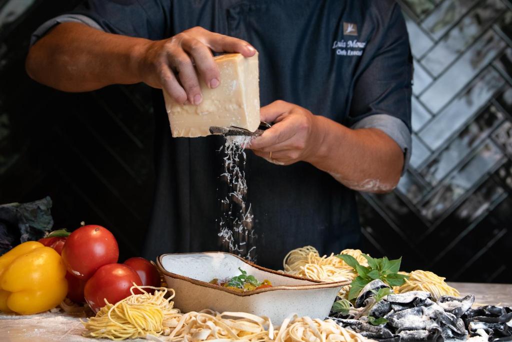 EPIC SANA Algarve Hotel šefpavārs rīvē sieru pār svaigi gatavotu pastu un dārzeņiem