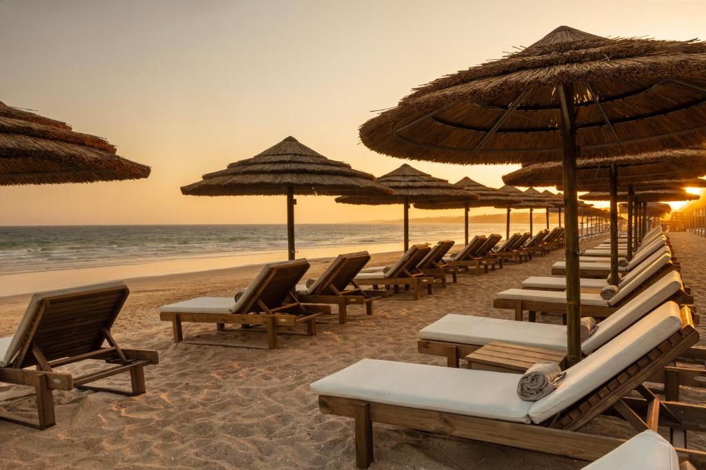 EPIC SANA Algarve Hotel pludmales zona ar koka atpūtas krēsliem un saulessargiem saulrietā.