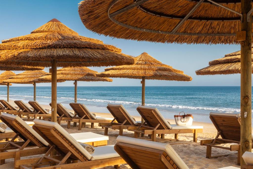 EPIC SANA Algarve Hotel pludmales zona ar salmu saulessargiem un koka zviļņiem pie okeāna.